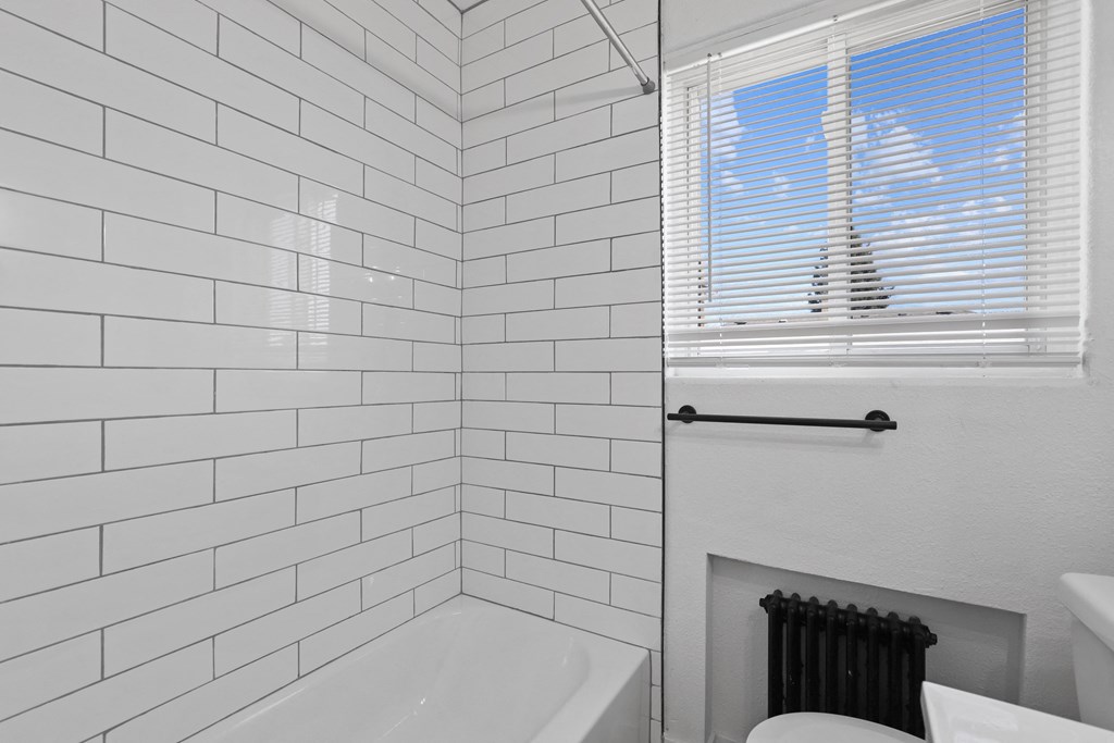a white bathroom with white tiled walls and a window
