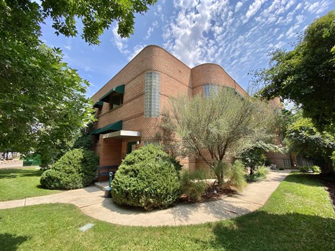 A large red brick building with a green awning and a circular driveway in front.