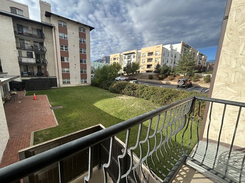 A balcony with a metal railing overlooks a grassy area and buildings.