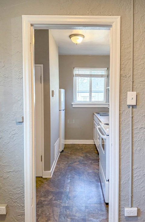 A white doorway leads to a kitchen with a dishwasher and a window.