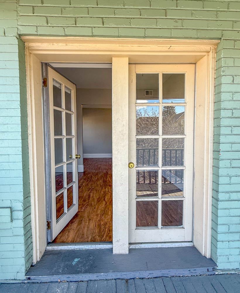 A white door with a glass window is open to a room with a wooden floor.