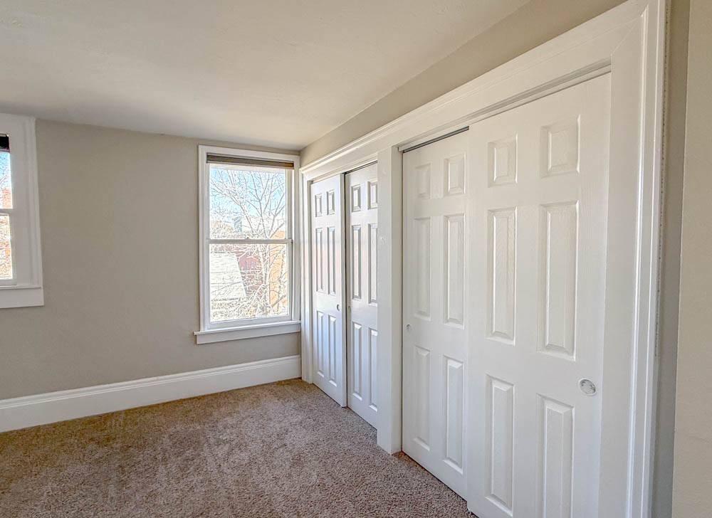 A room with a carpeted floor, a window, and a white door.