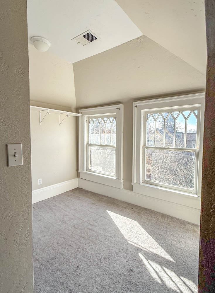 A room with two windows and a light switch on the wall.