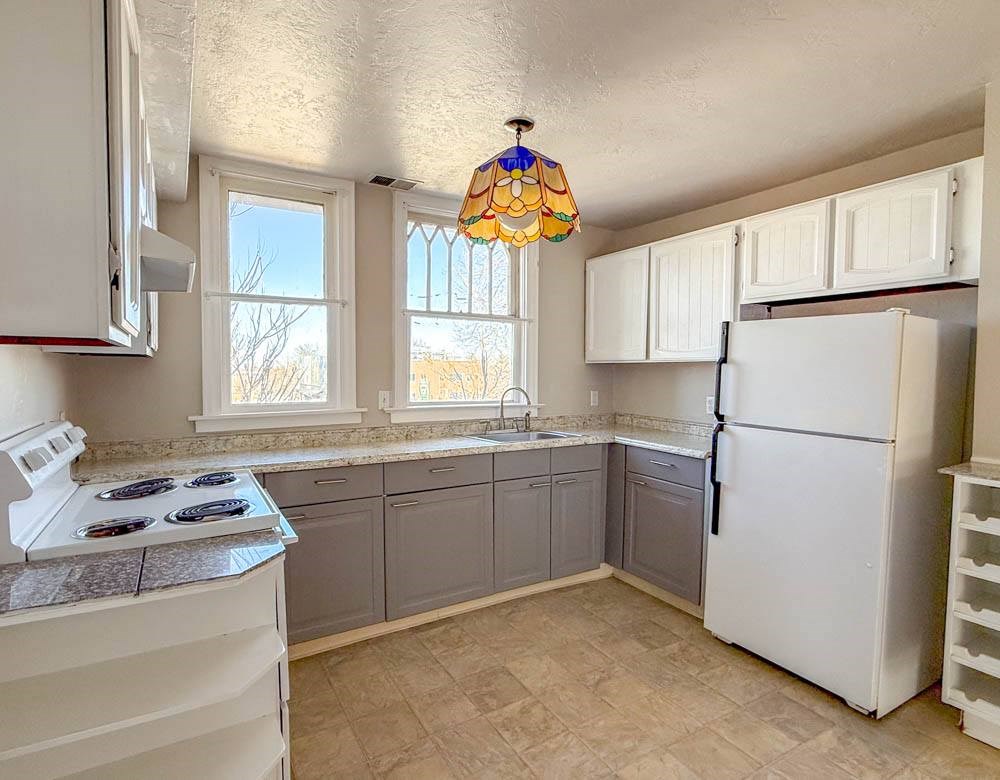 A kitchen with a white stove, white refrigerator, and a tiled floor.