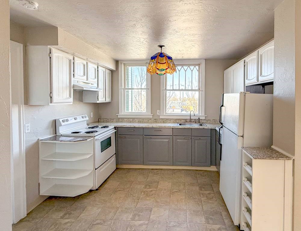 A kitchen with white appliances and a tiled floor.