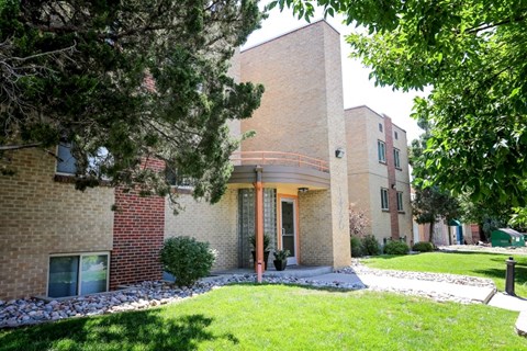 A building with a red brick wall and a glass door is surrounded by trees.