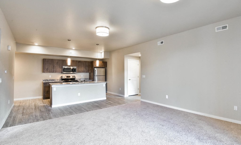 an empty living room with a kitchen with a stove and refrigerator