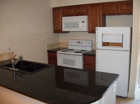 A kitchen with a black counter top and white appliances.