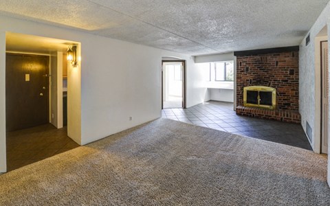 an empty living room with a brick fireplace and a carpet
