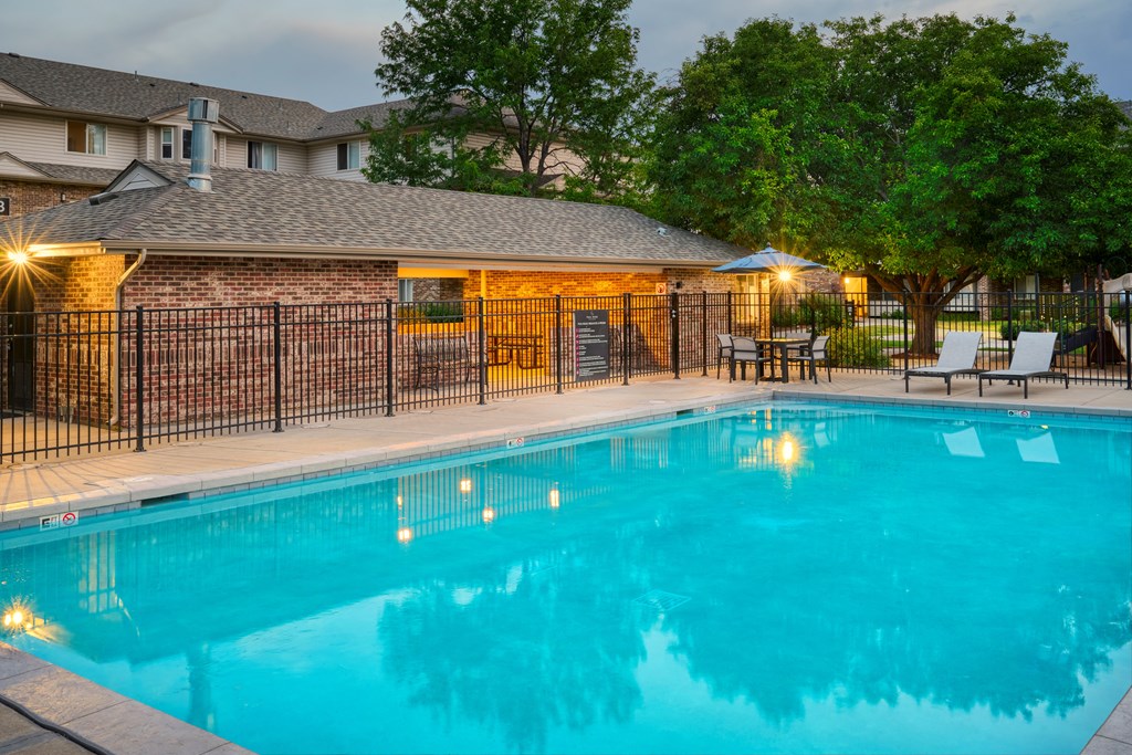 A pool surrounded by a black fence and a building in the background.