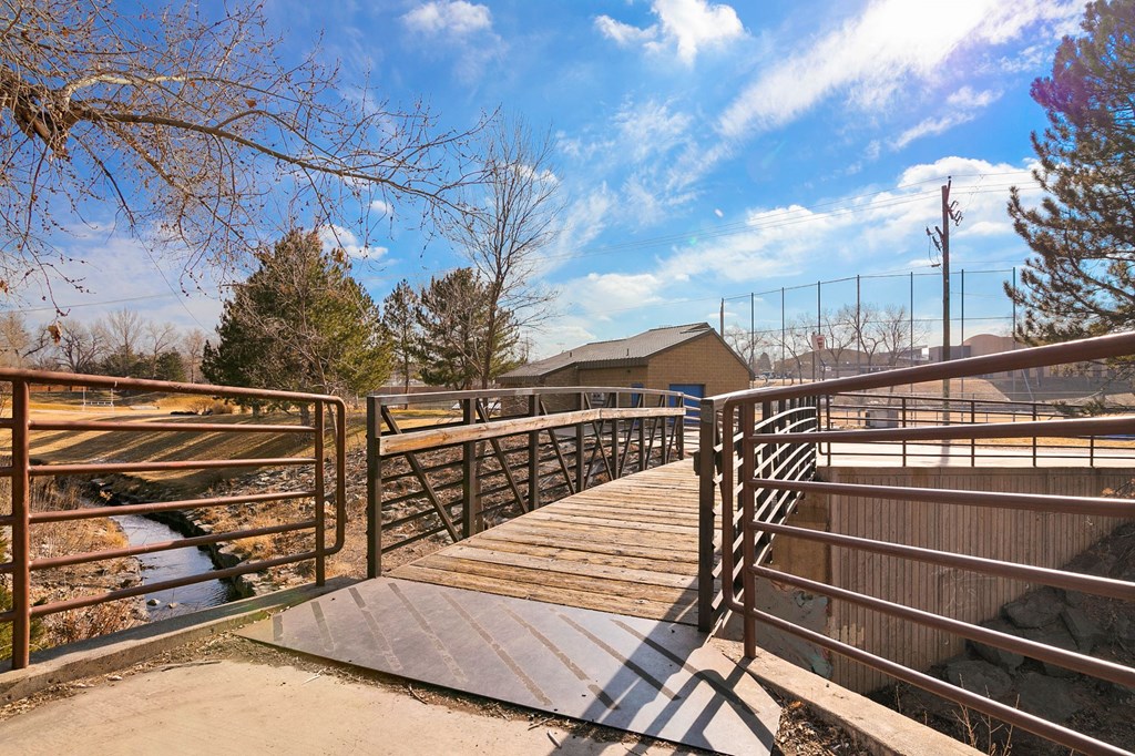 a bridge over a stream with a baseball field in the background
