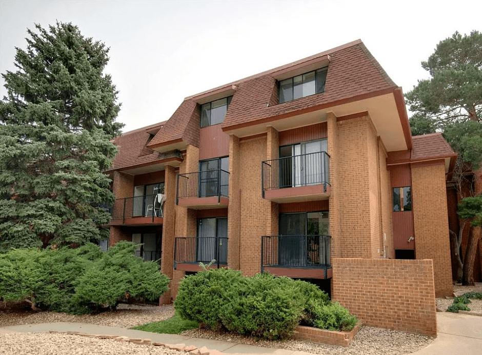 A brick building with a balcony and a small garden in front.