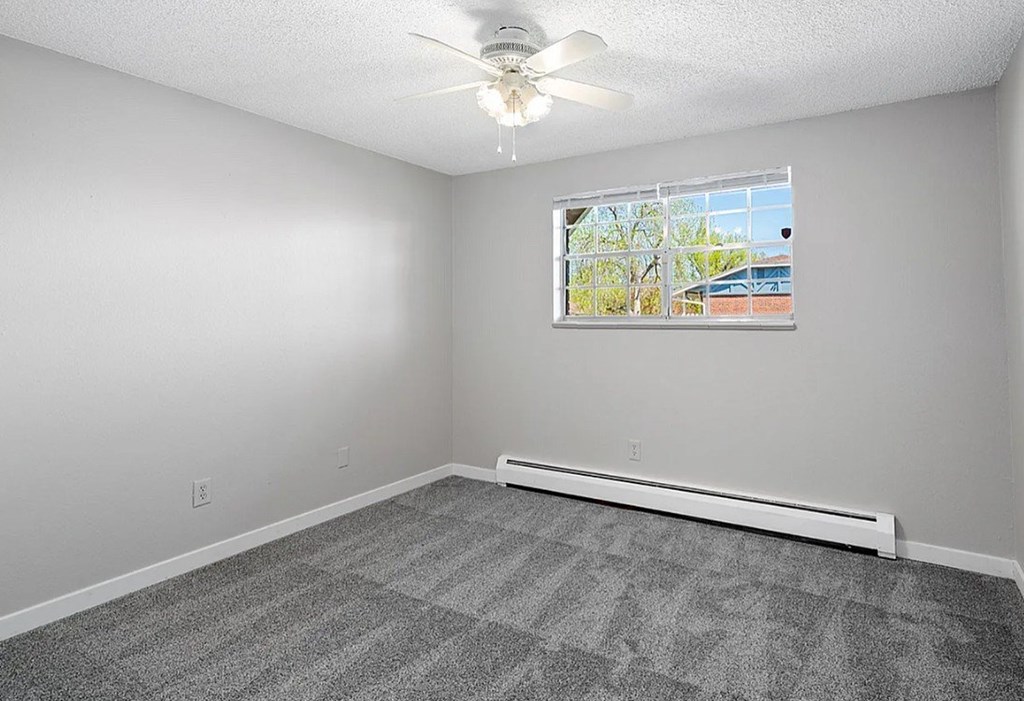 A room with a ceiling fan and a window with a view of a building outside.