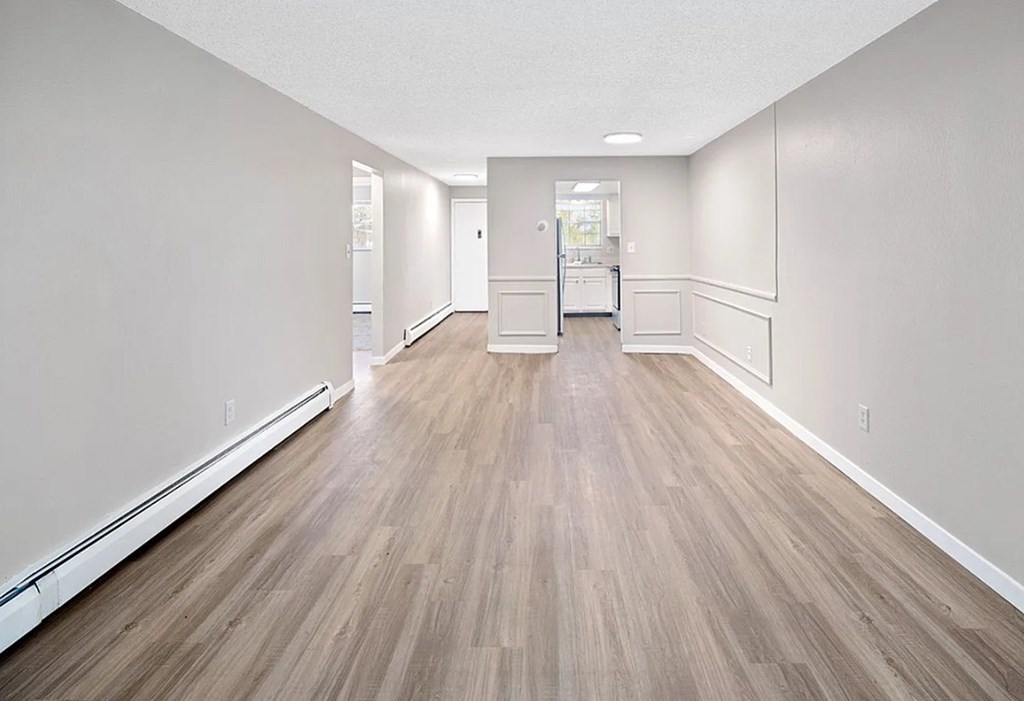 A long, empty hallway with wood flooring and white walls.