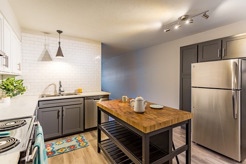 A kitchen with a wooden table and a stainless steel refrigerator.