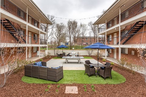 A courtyard with a table, chairs, and umbrellas surrounded by apartment buildings.