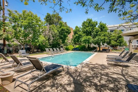 A pool surrounded by lounge chairs and trees.