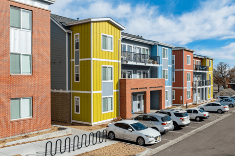 A row of colorful apartment buildings with cars parked in front.