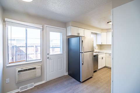 A kitchen with a refrigerator, cabinets, and a window.