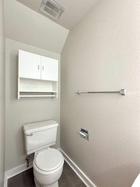 A white toilet in a small bathroom with a shelf above it.
