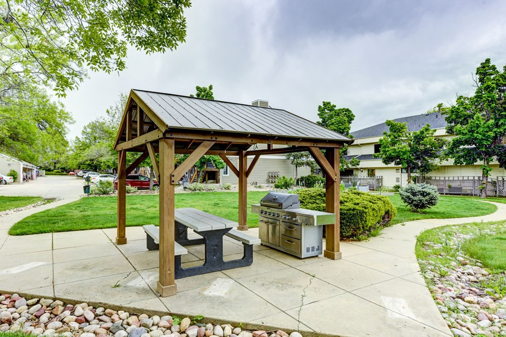A wooden pavilion with a black roof and a picnic table in front of a grassy area.