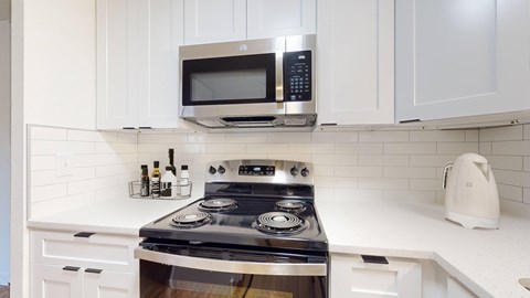 A modern kitchen with a stove, microwave, and white cabinets.