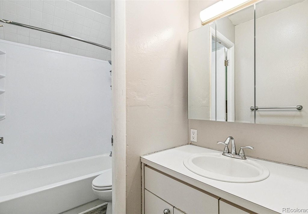 A white bathroom with a sink, mirror, and toilet.