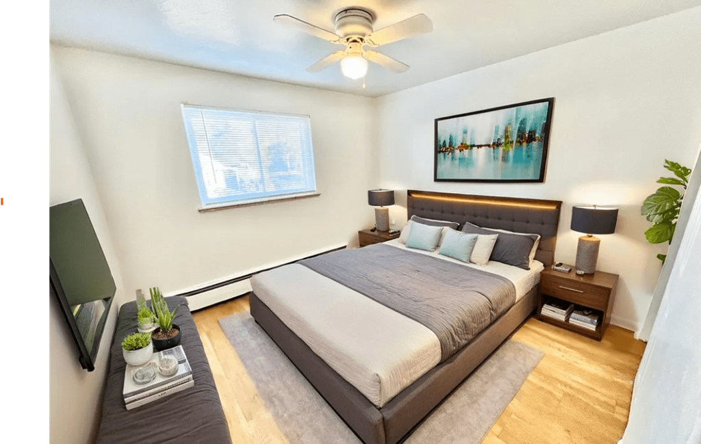 A bedroom with a large bed, a ceiling fan, and a painting on the wall.