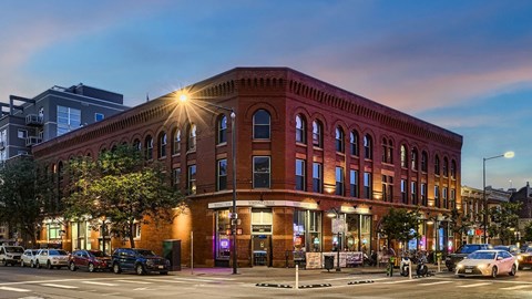 A red brick building with a lit up window on the corner.