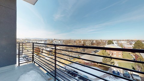 A balcony with a metal railing overlooks a parking lot and buildings.