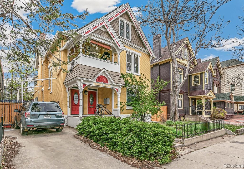 A yellow house with a red door is surrounded by a black fence.