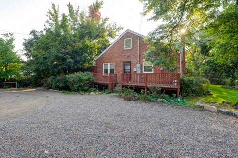 a red brick house with a gravel driveway and trees