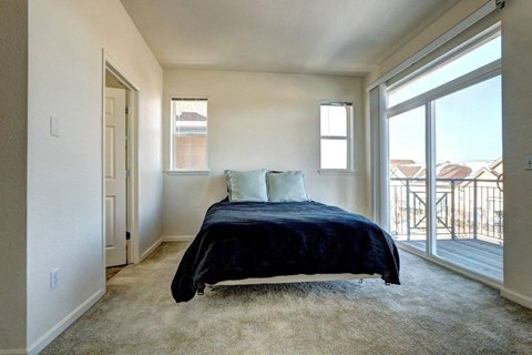 A bedroom with a bed, carpet, and sliding glass doors.