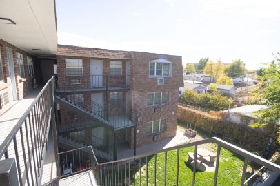 A balcony overlooks a brick building and a green lawn.