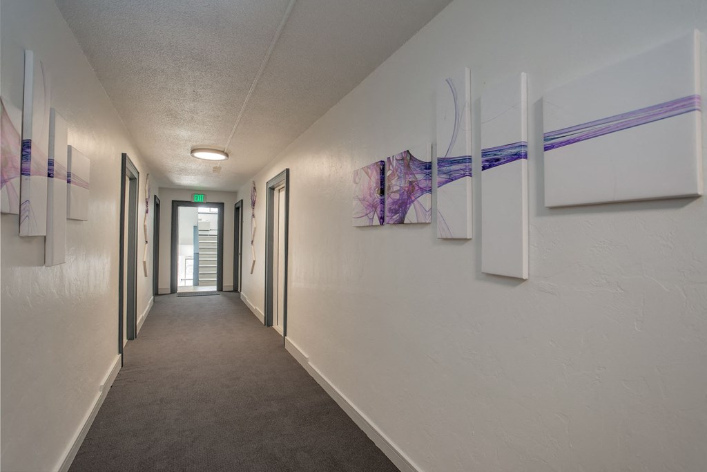 a hallway with paintings on the wall and a corridor leading to a door