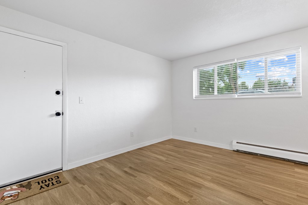 A room with a white door, a window with blinds, and a wooden floor.