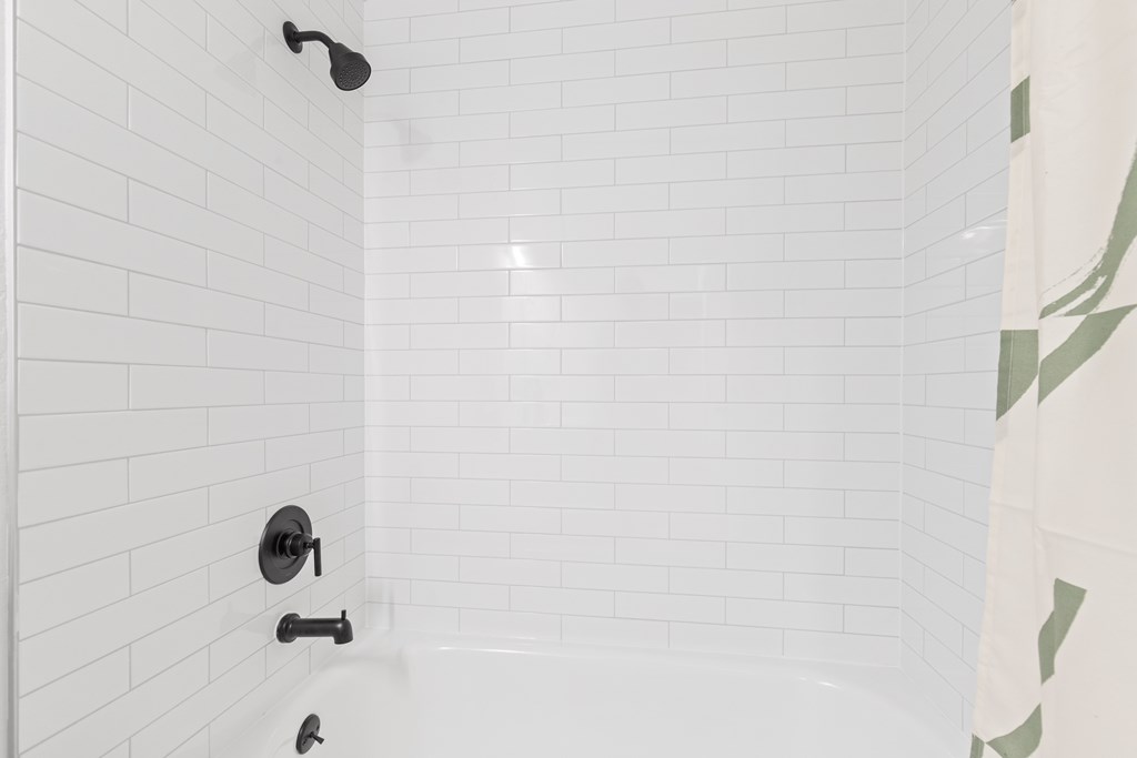 A white tiled shower with a black faucet and shower head.