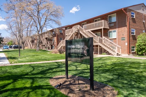 A sign for the Estates Village Apartments stands in a grassy area in front of a brick building.