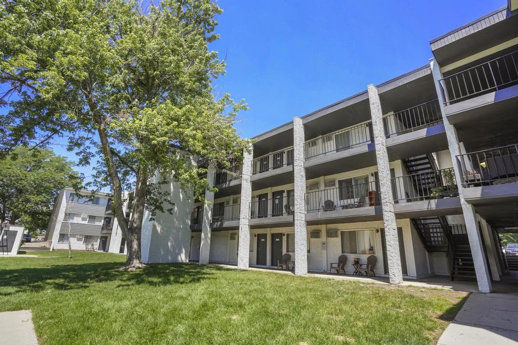 the exterior of an apartment building with grass and trees at The Iris Apartments, Arvada, CO
