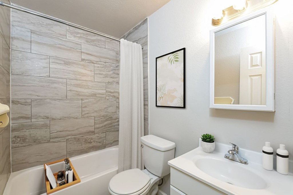 A bathroom with a white toilet, a white sink, and a grey tiled shower.