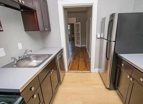 A kitchen with a sink, refrigerator, and wooden floors.