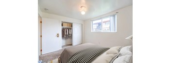 A bedroom with a bed, a window, and a closet with clothes hanging.
