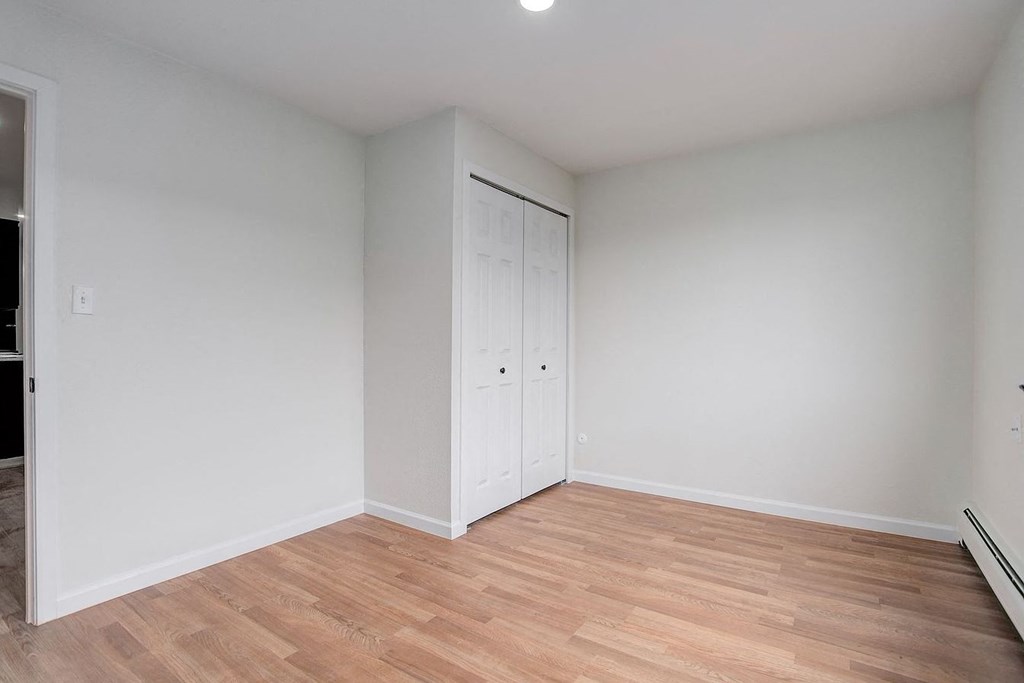 a living room with white walls and wood flooring and a closet