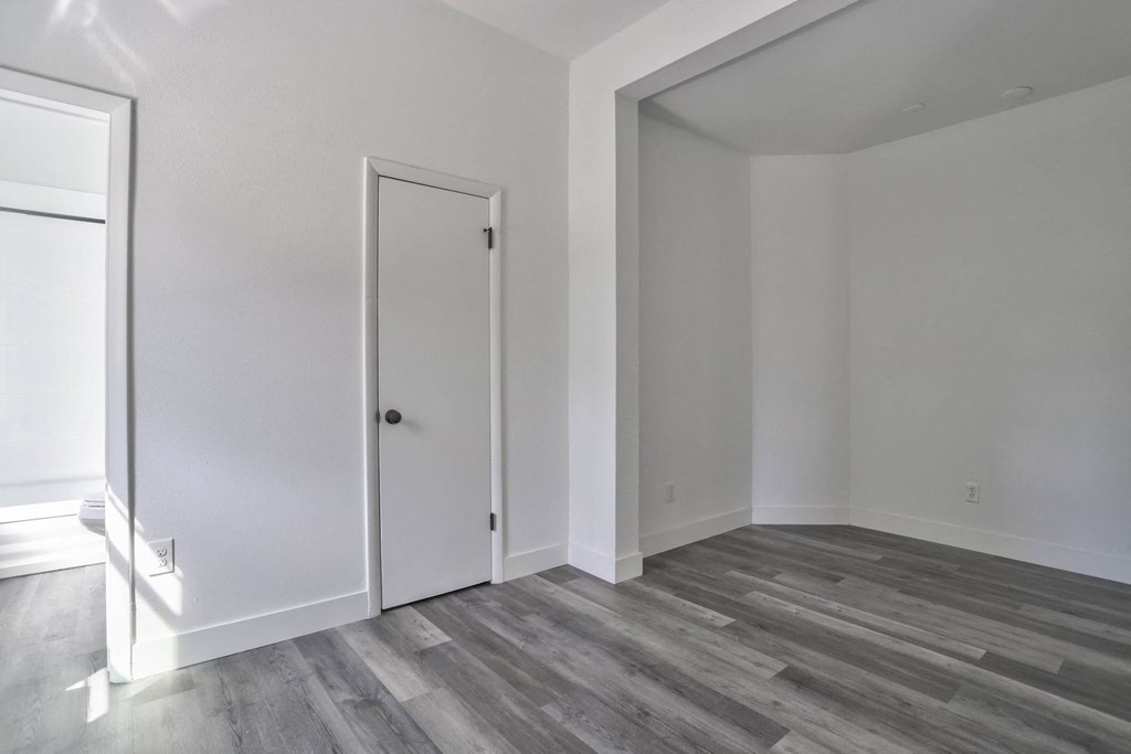 a bedroom with white walls and wood flooring and a door