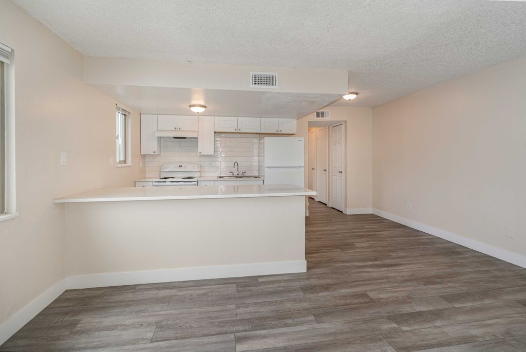 an empty living room with a kitchen with a counter top and