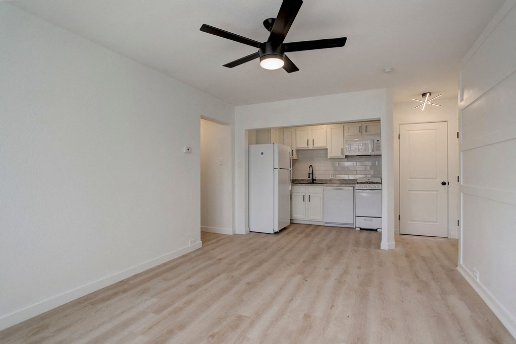 an empty living room with a ceiling fan and a kitchen