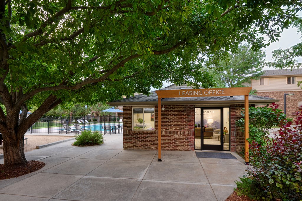 A leasing office is surrounded by greenery and has a pool in the background.