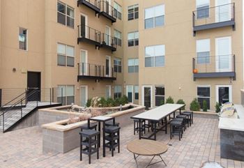 A patio area with tables and chairs is surrounded by apartment buildings.