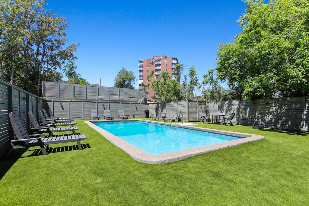 a backyard with a pool and lounge chairs in front of a fence