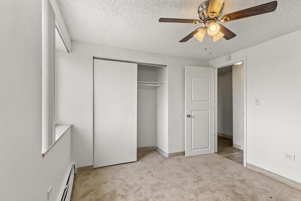 an empty living room with a ceiling fan and a closet